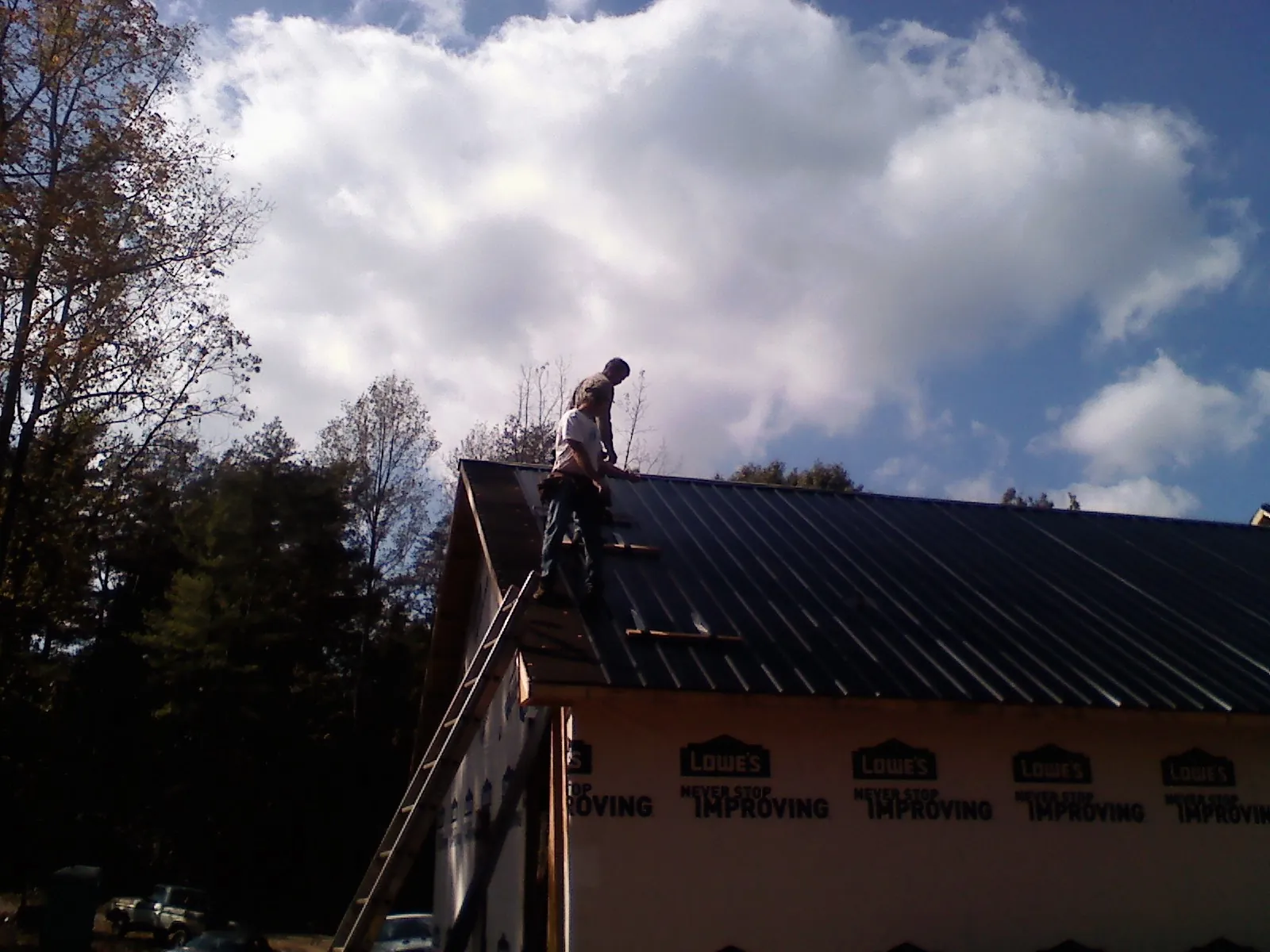 Roofer fastening dark metal panels high against a cloudy sky, from a Roof Inspection job in Warren